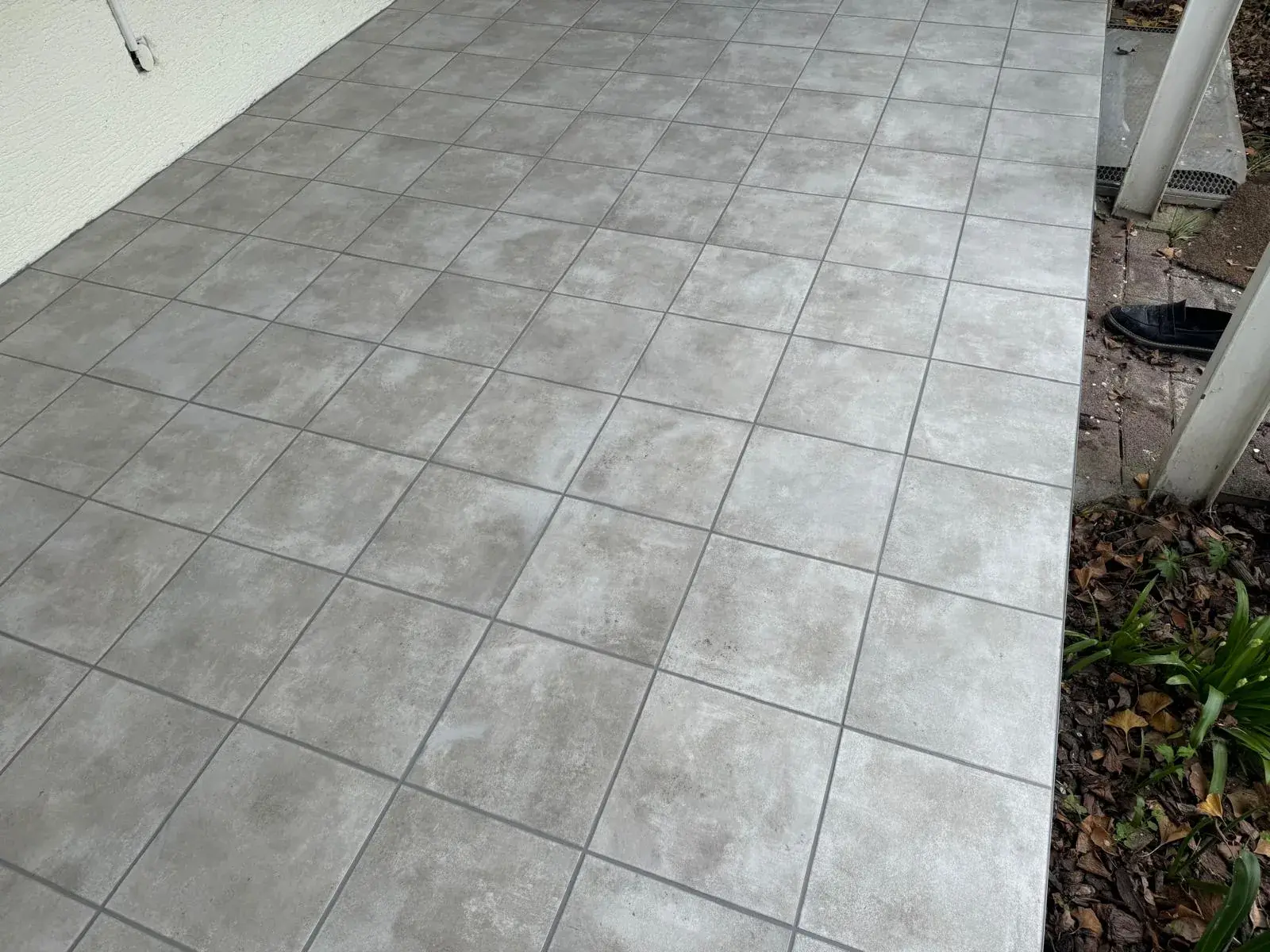Graue quadratische Bodenfliesen auf einer Terrasse entlang einer hell verputzten Hauswand